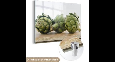 MuchoWow® Glasschilderij 120x80 cm - Schilderij acrylglas - Drie hoofden van een artisjok of Cynara scolymus gelegen op een houten plank - Foto op glas - Schilderijen